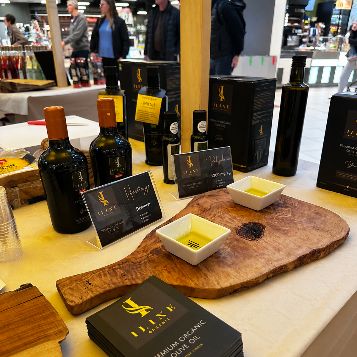 Iline Organic Degustationsstand im Geschäft mit verschiedenen Olivenölen, zwei Probeschalen auf Olivenholz und Informationsbroschüren.
