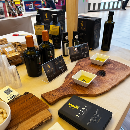 Iline Organic Degustationstisch mit Bio-Olivenölflaschen, schwarzen Produktboxen, zwei Probeschalen und Broschüren im Ladengeschäft.
