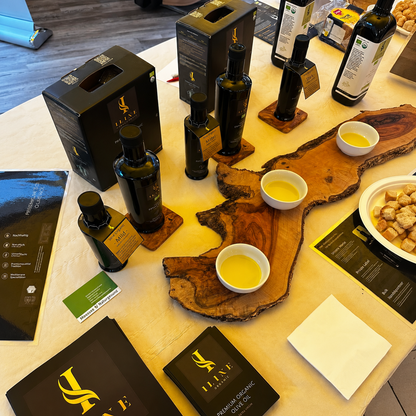 Iline Organic Degustationstisch mit Bio-Olivenölflaschen, Produktboxen und Probeschalen auf Olivenholzbrettern sowie Brot für die Verkostung.